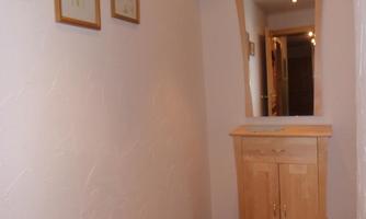 A narrow hallway with a wooden wardrobe and a mirror. Framed pictures are hanging on the wall, and the floor is carpeted.
