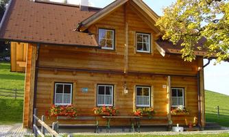 A beautiful wooden house with a red roof, surrounded by green meadows. In front of the house, there are flower boxes with colorful flowers.