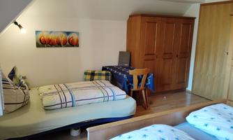 A cozy room with two beds and a wooden wardrobe. A picture of flowers hangs on the wall, and there is a small table with chairs.