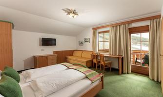 A comfortable hotel room with two beds and green carpets. There is a sofa, a table, and a balcony with a view outside.