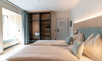 A modern hotel room with two beds and bright colors. Large windows provide plenty of daylight and a welcoming atmosphere.
