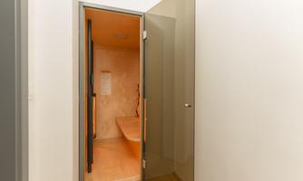 A modern sauna area with warm wooden tones and soft lighting. The glass door opens to a tranquil space.