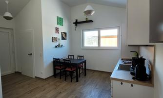 A modern, bright room with a small kitchenette and a dining area. The space has a wooden floor and large windows that let in plenty of light.