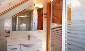 A modern bathroom with a white sink and wooden details. The walls are tiled and there is a shower cabin with a glass partition.