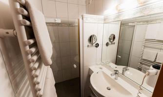 A modern bathroom with a shower, a sink, and a towel rack. The walls are tiled, and the room feels bright and clean.