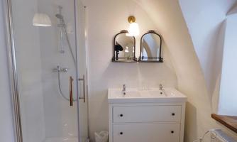 A modern bathroom with a glass shower and an elegant double sink. The walls are light, and the furnishings are simple and functional.