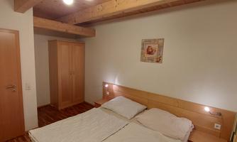 A simple bedroom with a double bed and wooden details. A small picture hangs on the wall, and there is a wardrobe.