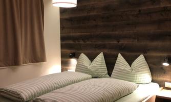 A cozy bedroom with a large bed and green pillows. The walls are made of wood and the lighting creates a pleasant atmosphere.