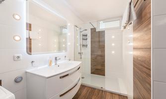 A modern bathroom with a large shower and an elegant sink. Walls in white and wood look create a bright and inviting atmosphere.