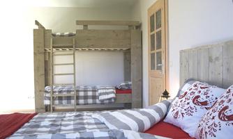 A modern bedroom with a bunk bed and a double bed. The bedding is in gray-white checks and red, and the room is bright and inviting.
