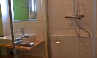 A modern bathroom with a shower and a sink. The walls are light, and the space feels clean and well-designed.