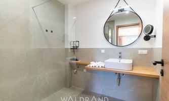 A modern bathroom with a glass shower and a minimally designed wooden vanity top. The large mirror and bright furnishings create an inviting atmosphere.