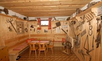 A rustic room with wooden walls and cozy seating. Various agricultural tools and historical items hang on the walls.