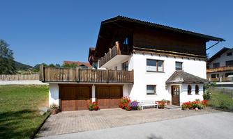 A beautiful house with two floors and a balcony. The entrance area is surrounded by flowers and there is a driveway with garage doors.