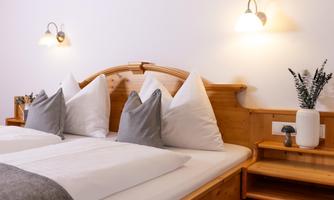 A cozy bedroom with a wooden bed and comfortable pillows. The room is warmly lit and has a modern, inviting atmosphere.