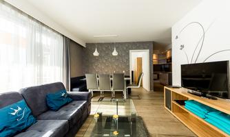 A modern living room with a comfortable sofa and a glass table. In the background, a dining area and an open kitchen can be seen.