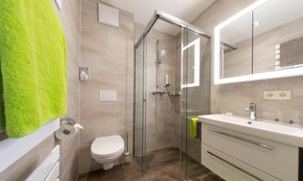 A modern bathroom with a glass shower and a simple sink. A green towel is attached to the wall, and the walls are in neutral tones.