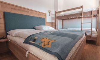 A cozy room with a double bed and a bunk bed. The walls are in warm wood tones.