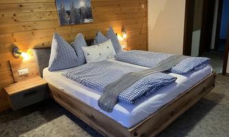 A cozy bedroom with a large bed and checked bed linen. The wooden walls have soft lighting and a picture of a snowy landscape.