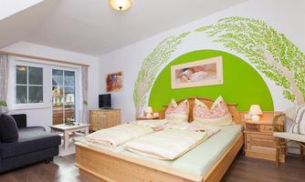 A cozy bedroom with a large double bed and a relaxing green wall design. The room also has a seating area and plenty of natural light.