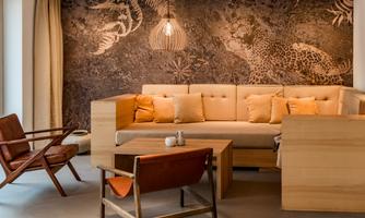 A modern living room with a comfortable sofa and wooden furniture. In the background is an interesting wall design featuring a leopard and plant motifs.