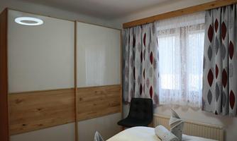 A bright room with modern furniture and large windows. The curtains are decorative and the bed is neatly draped with towels.