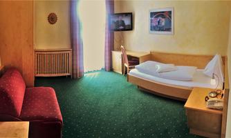 A simple hotel room with green carpet. There is a single bed, a television, and a seating area.