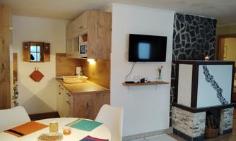 A modern kitchen and living room arrangement with wooden furniture. The space is bright and inviting, with a TV on the wall.