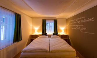 A cozy bedroom with a large bed and soft lighting. The walls are light, and one wall has a quote in elegant writing.