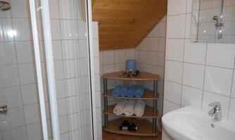 A bright bathroom with tiles and wooden details. There is a shower, a sink, and a shelf with towels.