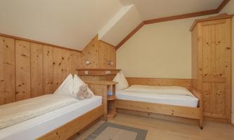A cozy room with two wooden single beds. The walls are paneled with wood and there is a small table between the beds.