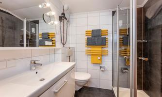 A modern bathroom with a sink, a shower, and a toilet. Striking yellow towel holders add a fresh accent.