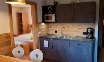 A bright and modern kitchen with an elegant wooden ceiling. There is a microwave, a coffee machine, and a cozy dining area.