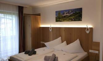 A modern bedroom with a large bed and bright wooden details. On the wall hangs a picture of a mountain landscape.