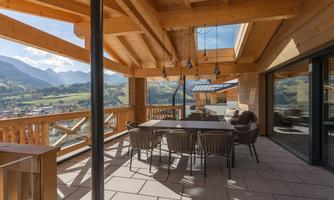 A beautiful balcony with wooden construction and a view of the mountains. A large dining table with chairs invites you to linger.