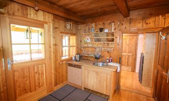 A cozy wooden kitchen with a modern sink and open shelves. The walls and floors are made of warm wood, creating an inviting atmosphere.