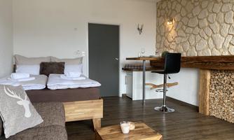 A cozy room with a double bed and a modern dining area. The walls are partially adorned with stones, creating a warm atmosphere.