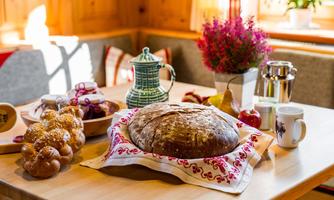A beautifully set table with fresh bread and pastries. Surrounding it are fruits and a teapot, all in a cozy setting.
