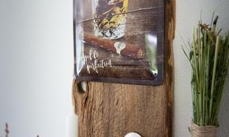 A rustic wooden shelf with a sign about whiskey and cigars. Below it is a candle and a heart-shaped decorative object.