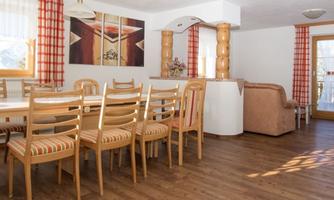 A bright living space with a large dining table and wooden chairs. Large windows provide plenty of light and a cozy atmosphere.
