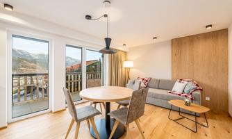 A modern living room with a cozy sofa and a round dining table. Large windows offer a view of the mountains.
