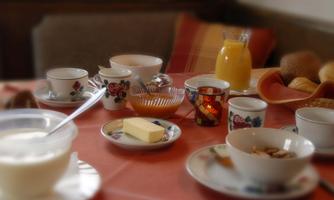 A breakfast table with various plates and cups. There is yogurt, butter, orange juice, and rolls.