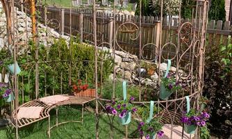 A decorative garden bench made of metal with potted flowers. It stands on green grass and is surrounded by plants.