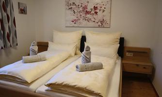 A cozy bedroom with two beds and fresh white bed linen. A decorative picture with floral motifs hangs on the wall.