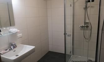 A modern bathroom with a shower and a sink. The walls are brightly tiled and there is a large mirror surface.