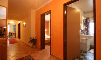 A bright hallway with orange walls and several doors. On the left side, a door leads to a bedroom, and on the right side, there is a bathroom.