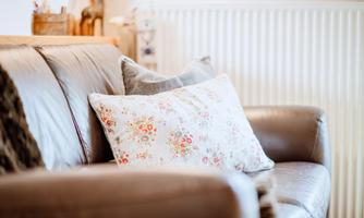 A cozy sofa with cushions. The cushion has a floral pattern and the surroundings feel inviting.