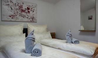 A cozy bedroom with two beds, elegant pillows, and towel-shaped decorations. On the wall hangs a modern artwork with floral motifs.