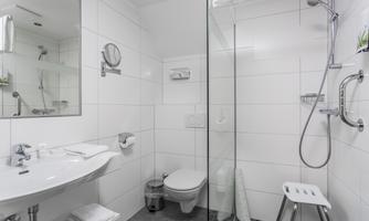 A modern bathroom with a glass shower and a white sink. The walls are tiled in light colors and there is a large mirror.