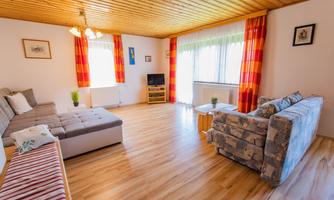 A bright living room with a wooden ceiling and a large window. The colorful curtains and furniture make the room appear friendly and inviting.